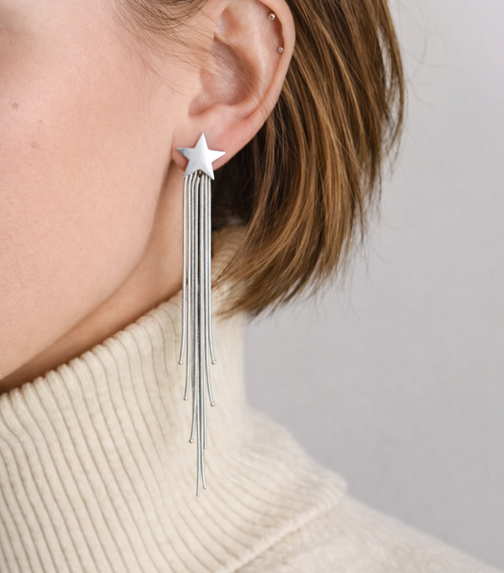 Silver star-shaped earring with tassels worn by a person against a neutral background