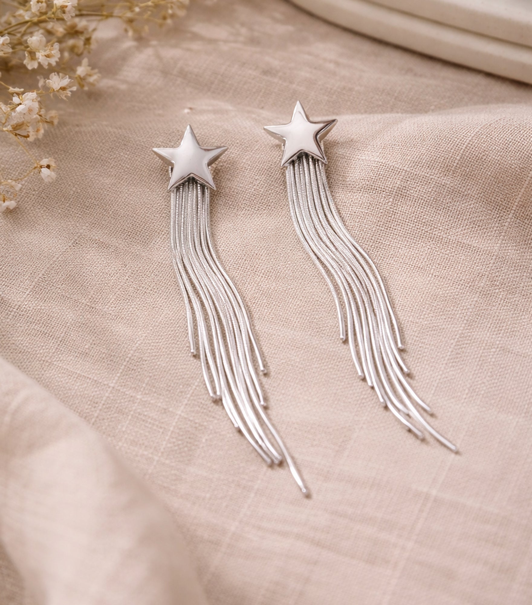 Silver star earrings with tassels on a beige fabric background