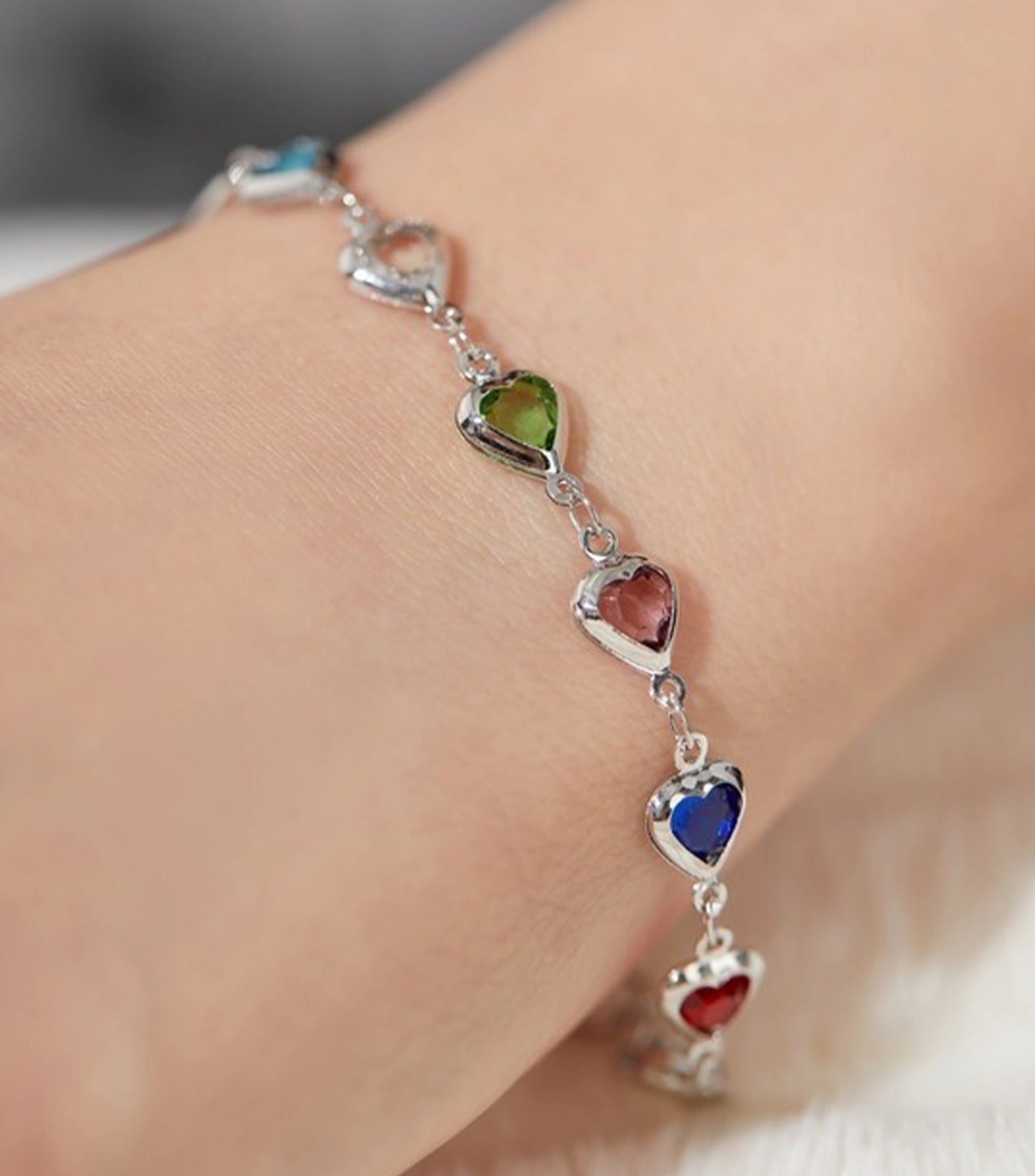 Bracelet with heart-shaped gemstones on a wrist against a neutral background
