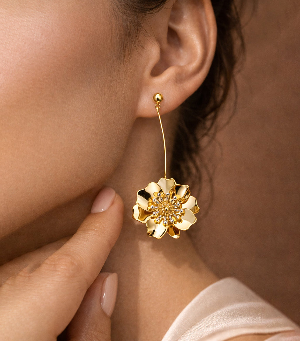 Gold floral earring worn by a person with a blurred background

