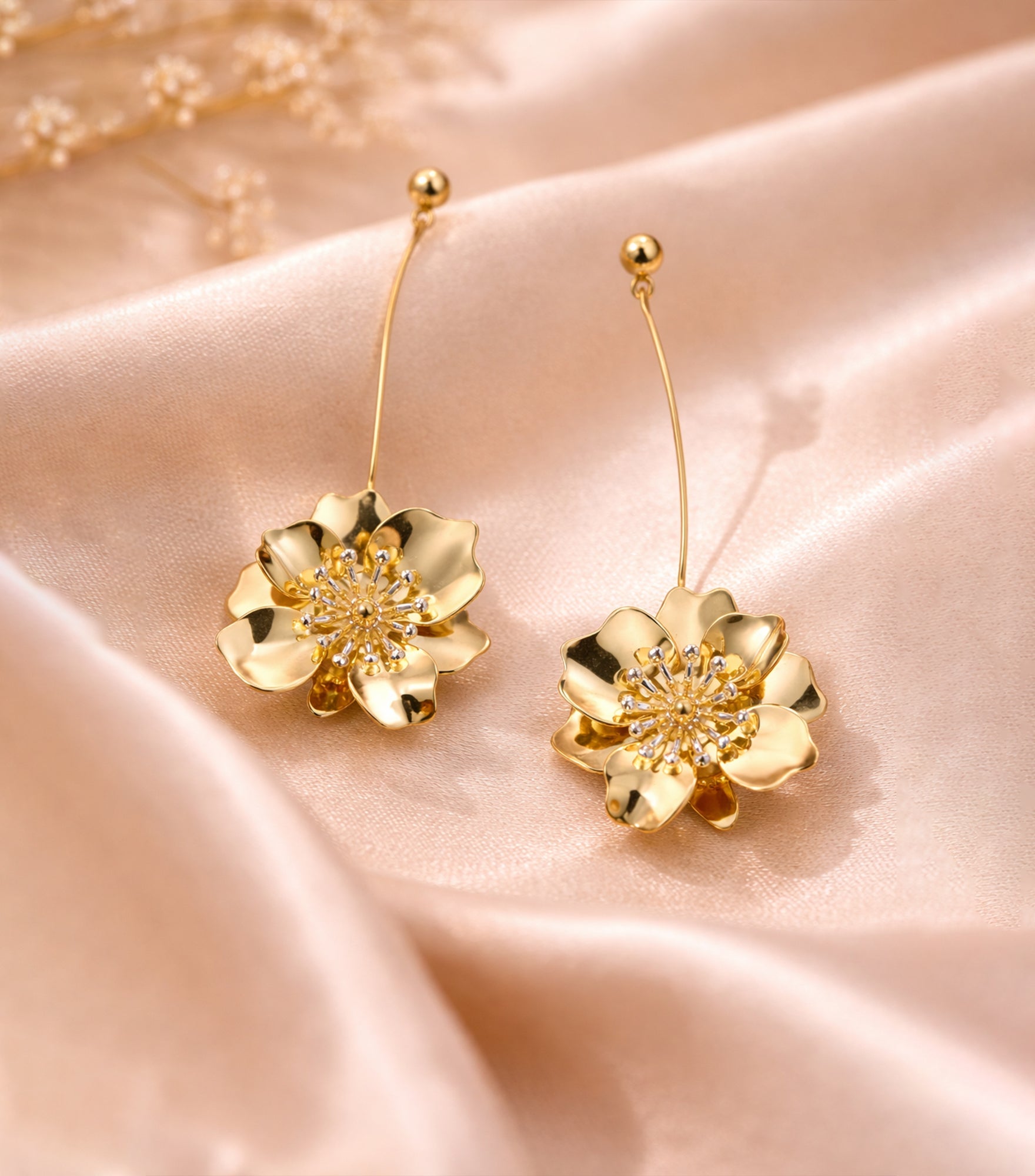 Gold flower-shaped earrings on a soft pink fabric background

