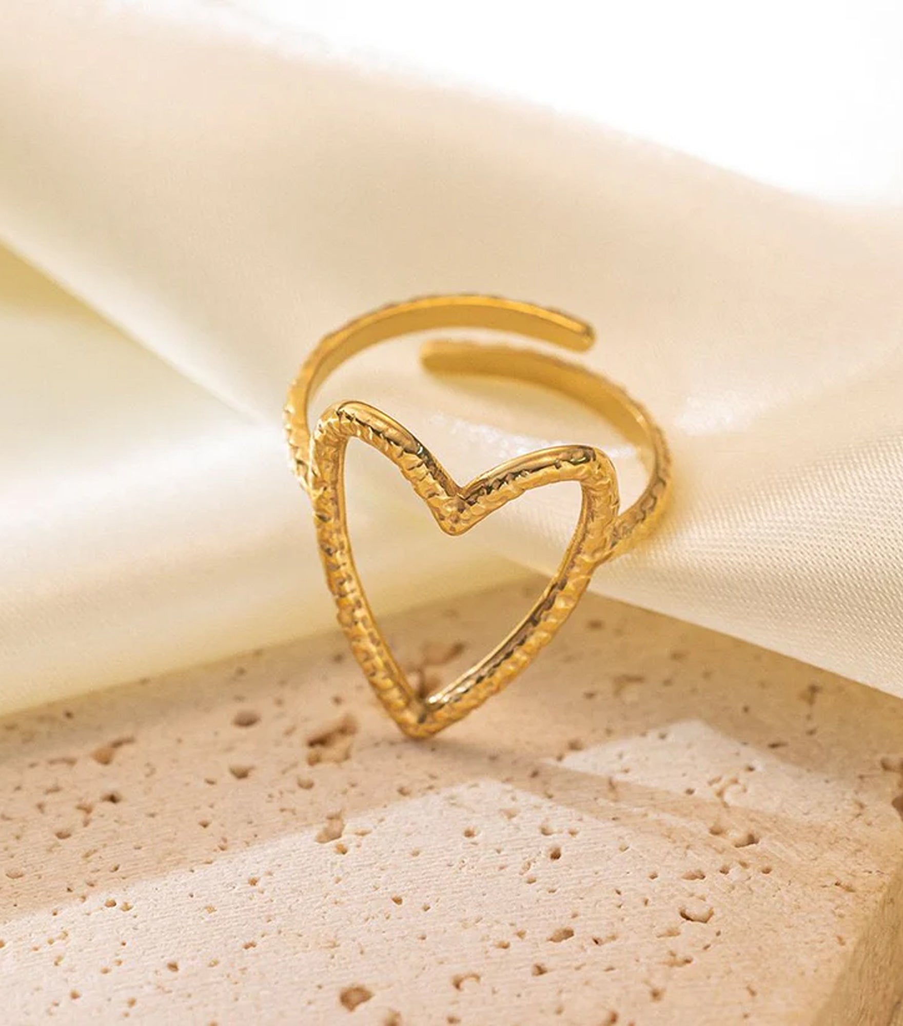 Gold heart-shaped ring on a beige fabric background
