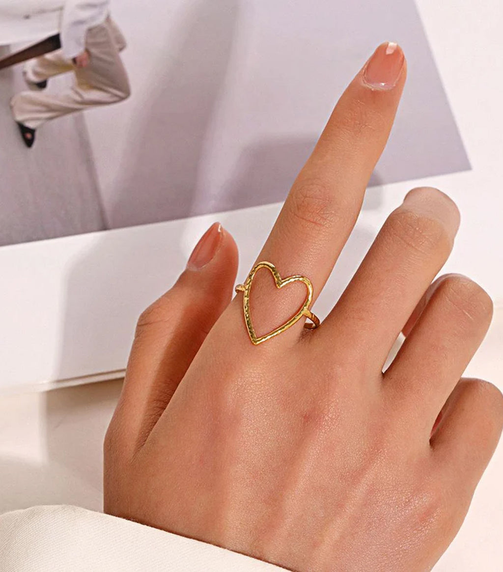 Gold heart-shaped ring on a finger with a blurred background