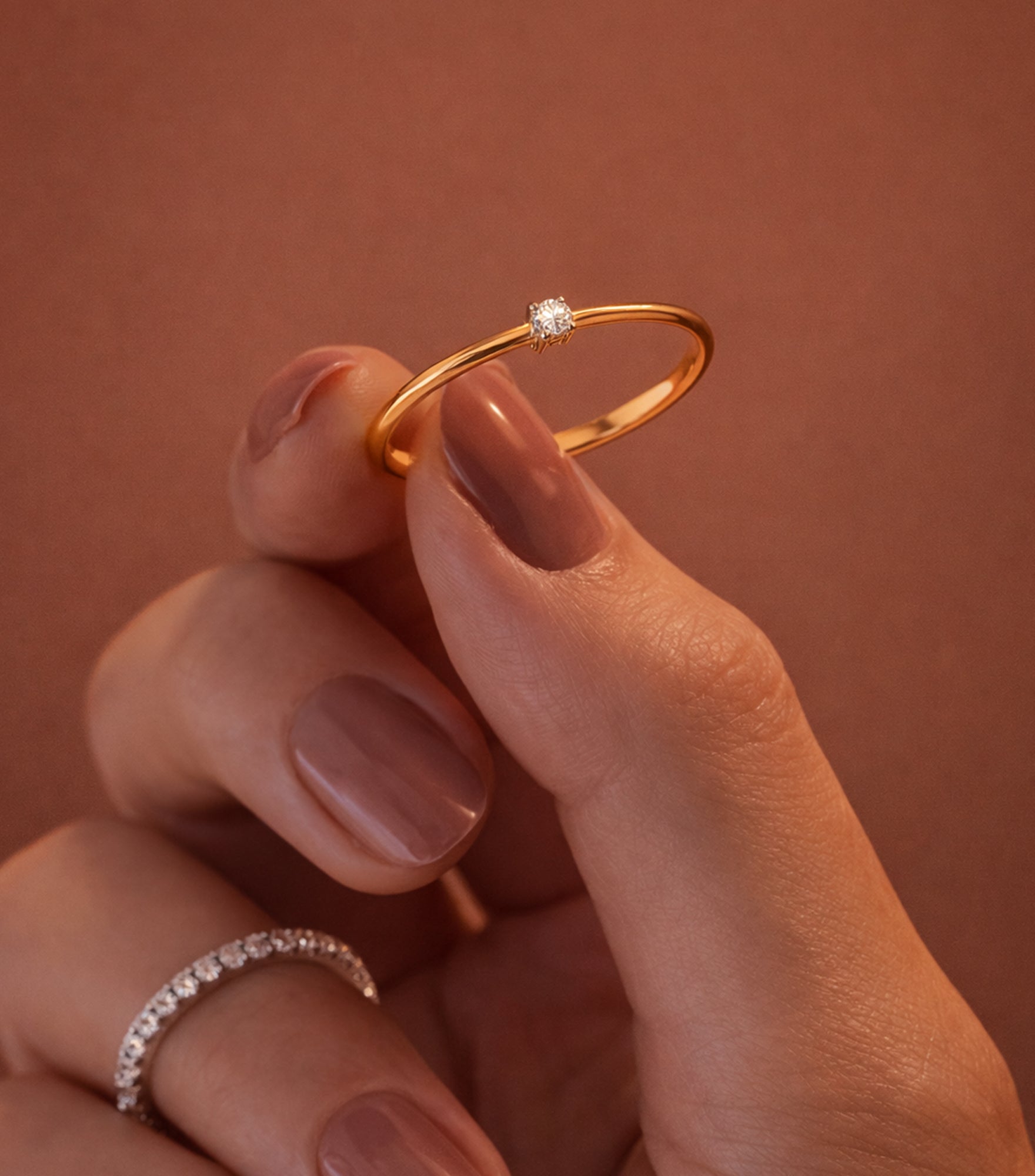 Gold ring with a diamond held between fingers against a warm brown background

