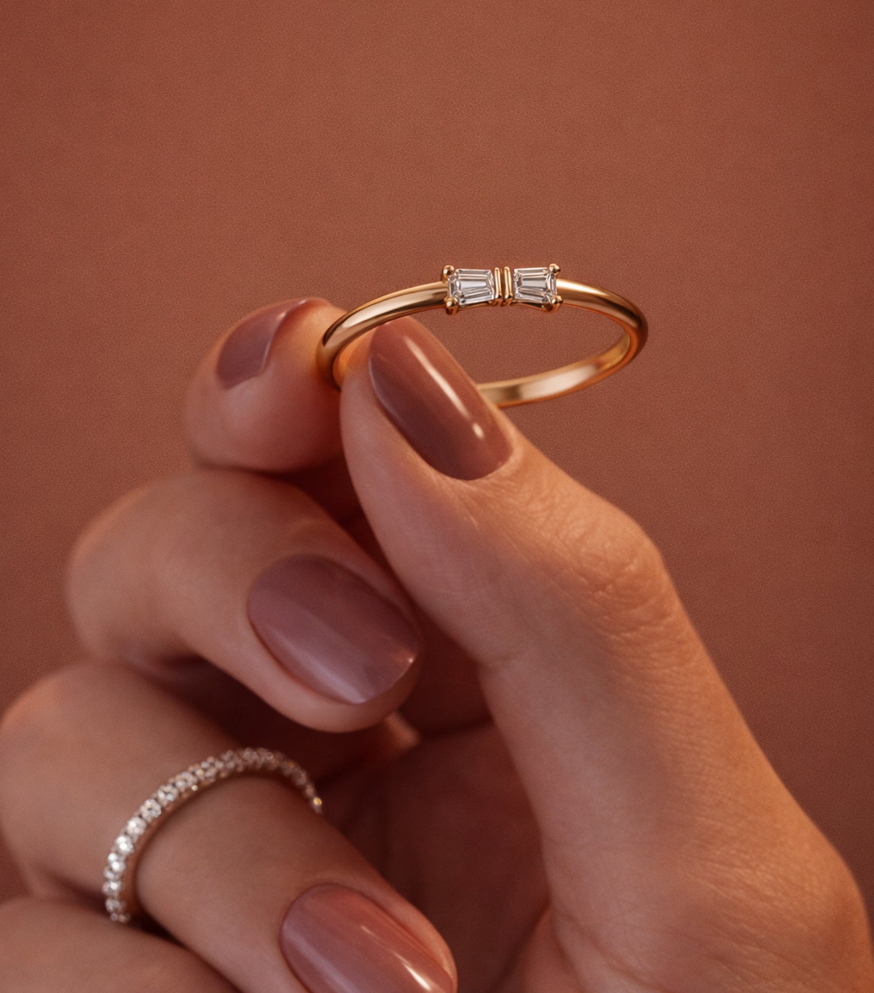 Gold ring with diamonds held by a hand against a brown background


