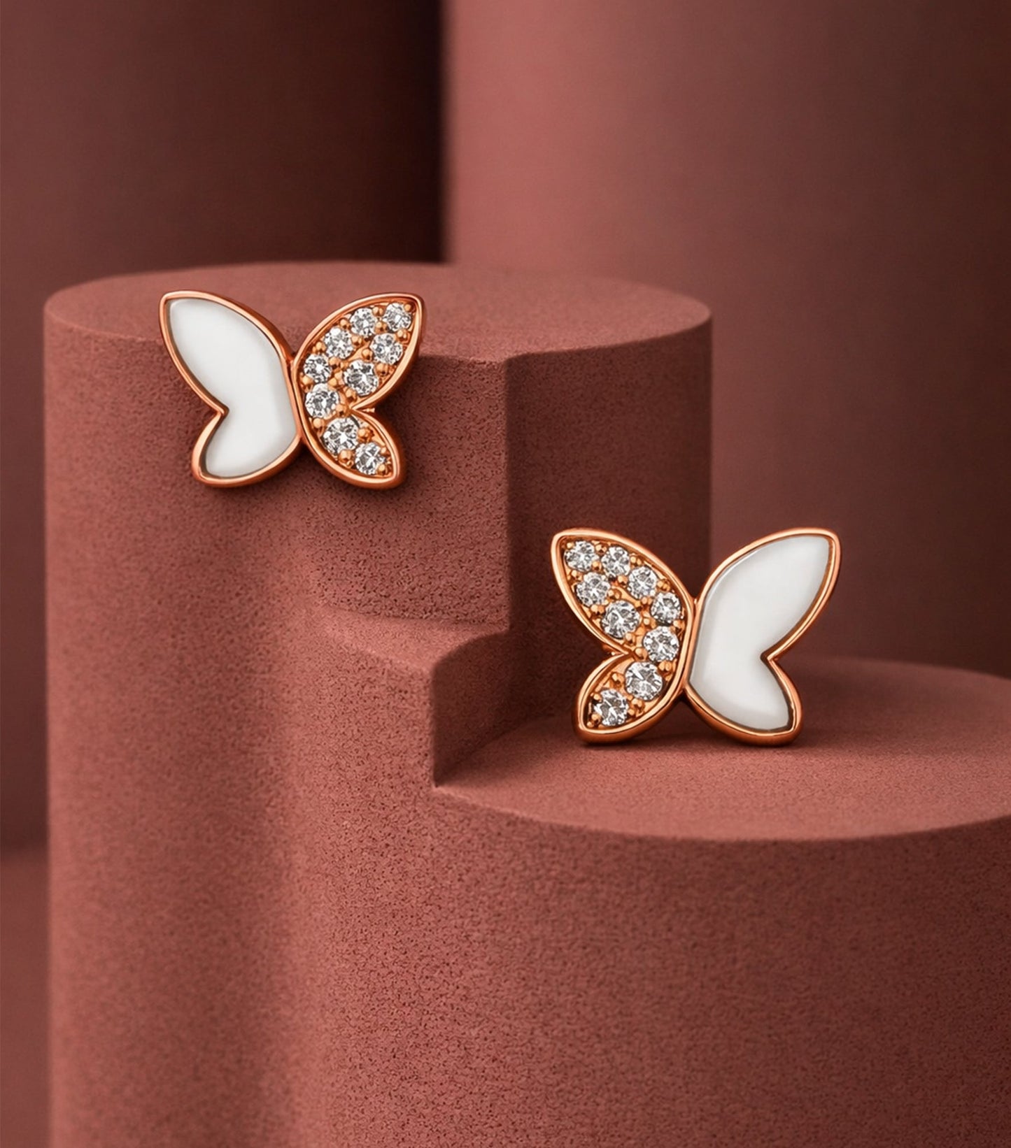 Butterfly-shaped earrings with gemstones on a brown pedestal

