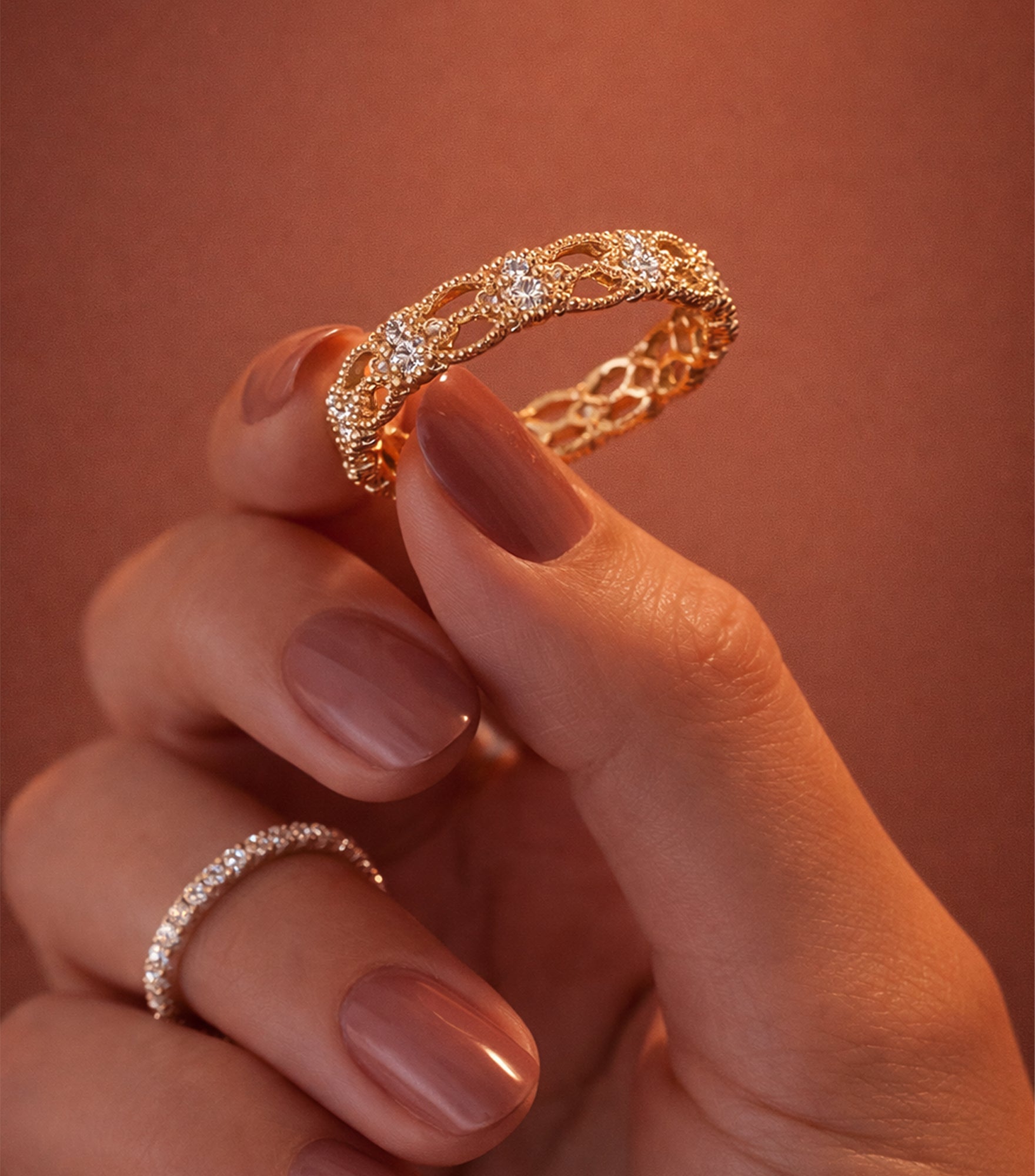 Gold ring with diamonds held by a hand against a warm brown background