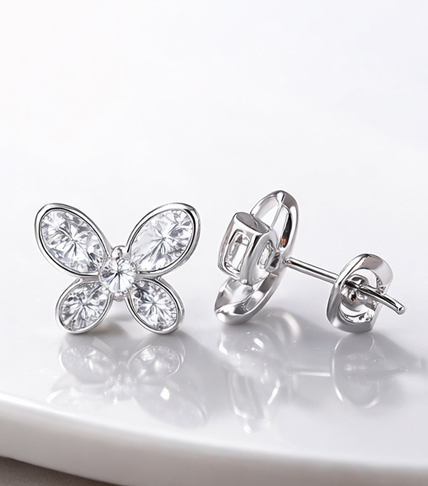 Butterfly-shaped silver earrings with clear gemstones on a white background

