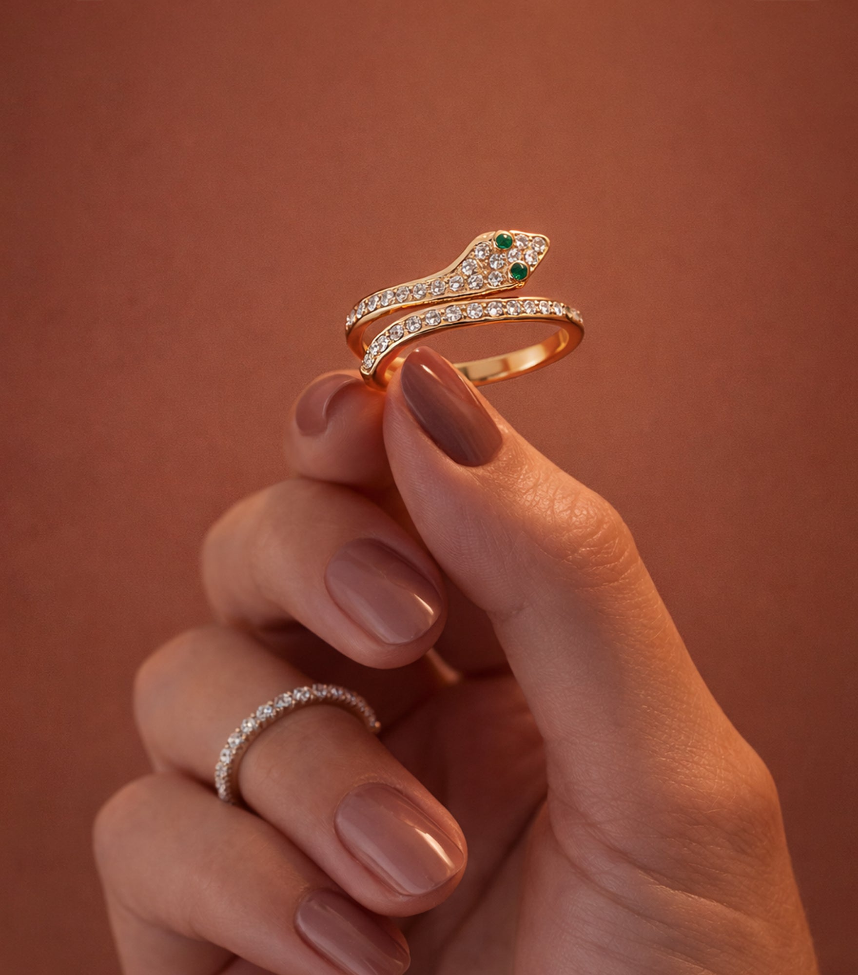 Hand holding a gold ring with green gemstones against a warm-toned background

