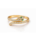 Gold snake-shaped ring with emerald eyes and clear gemstones on a white background

