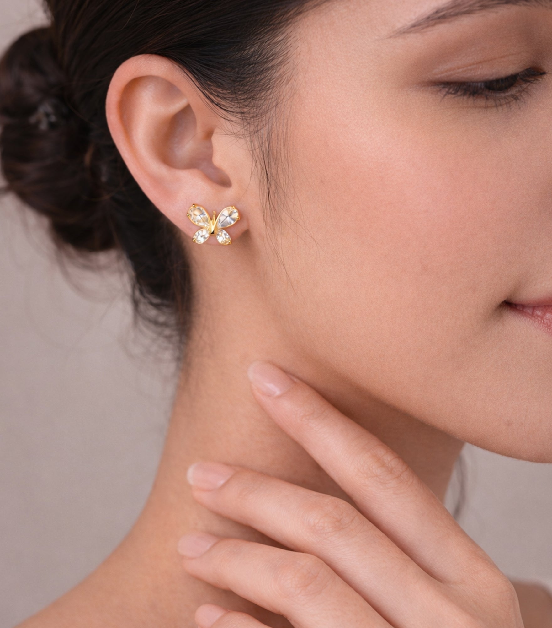 Close-up of a woman wearing butterfly-shaped earrings with a neutral background